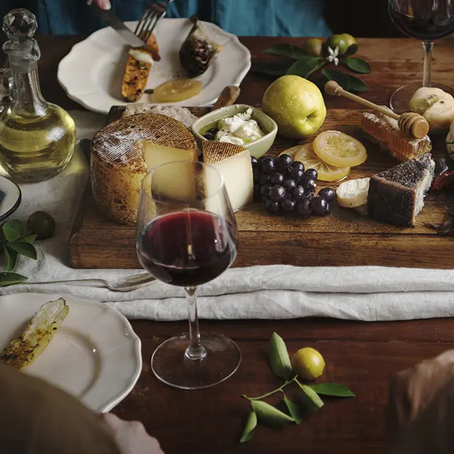 Et skjærebrett dandert med oster og tilbehør og vinglass rundt på et bord.