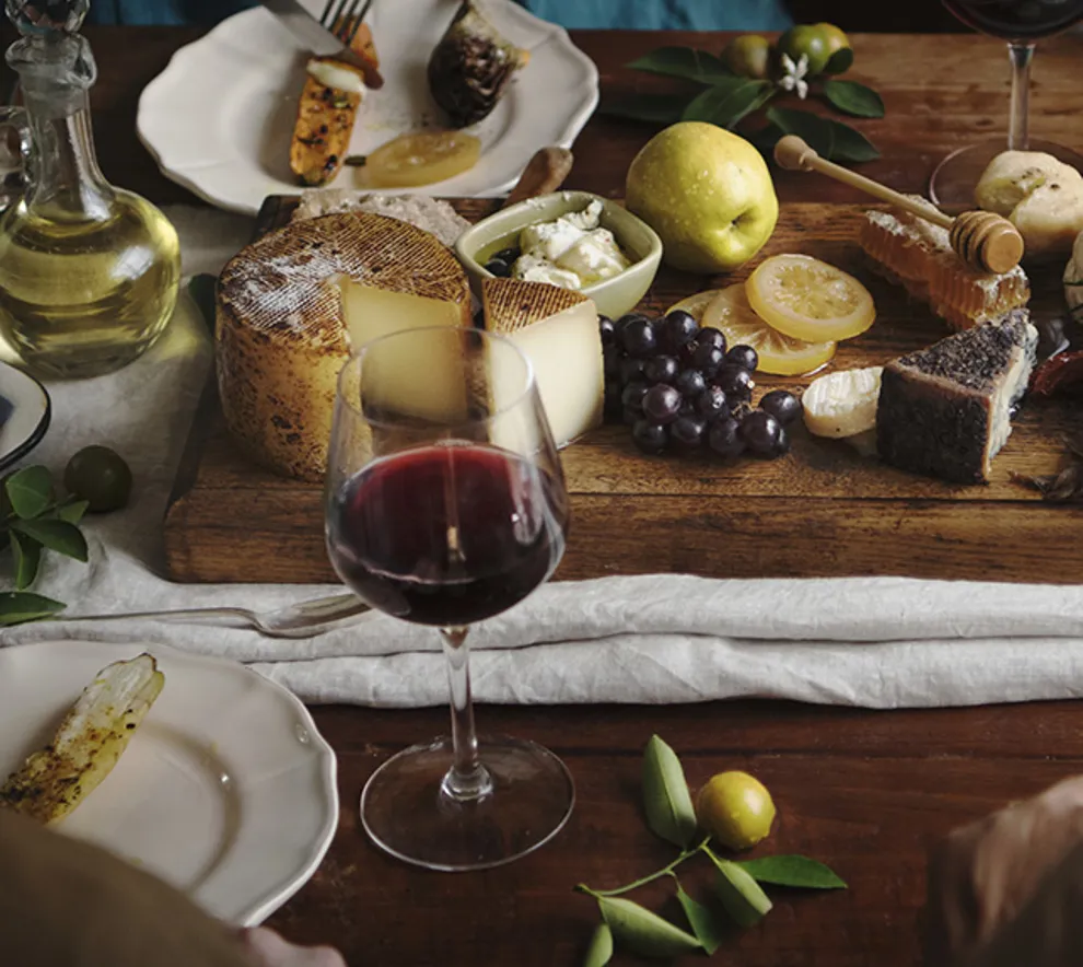 Et skjærebrett dandert med oster og tilbehør og vinglass rundt på et bord.