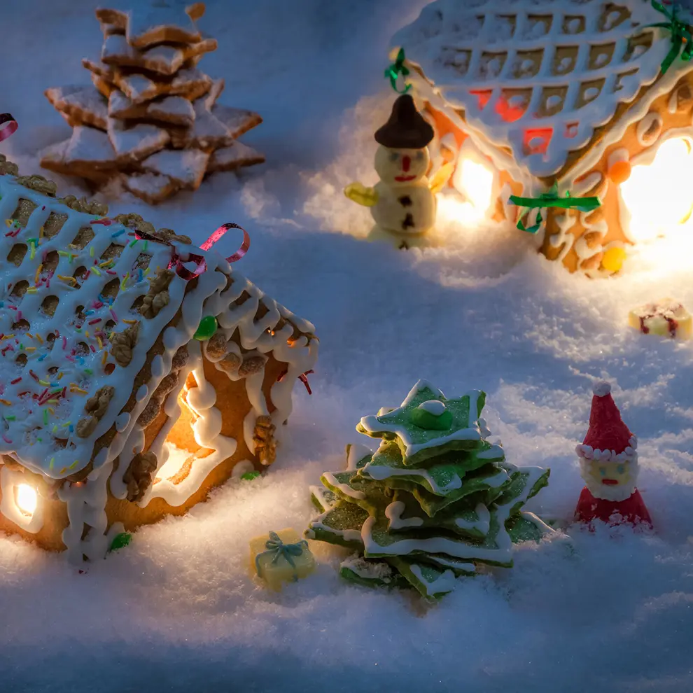 Opplyste pepperkakehus med julepynt, juletre og nisse i en snødekt pepperkakeby.