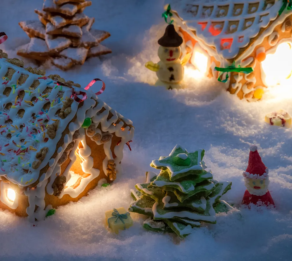 Opplyste pepperkakehus med julepynt, juletre og nisse i en snødekt pepperkakeby.