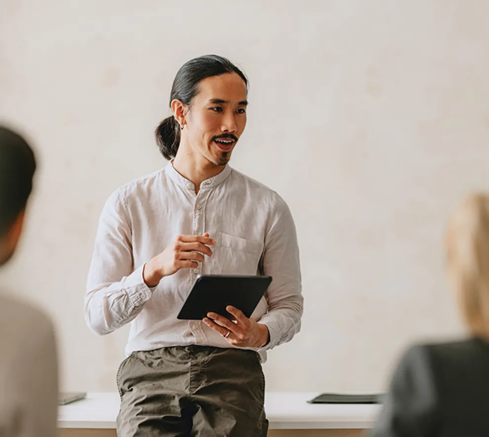 Mann holder presentasjon med nettbrett foran gruppe – effektiv kommunikasjon og historiefortelling. Spør ChatGPT