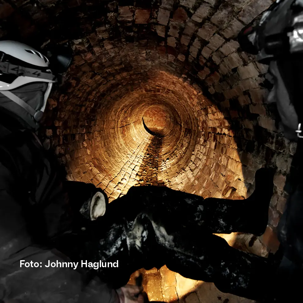 Underjordisk tunnell belyst av hodelykten til en person i forgrunnen.