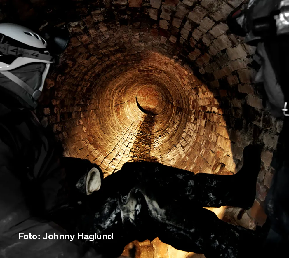 Underjordisk tunnell belyst av hodelykten til en person i forgrunnen.