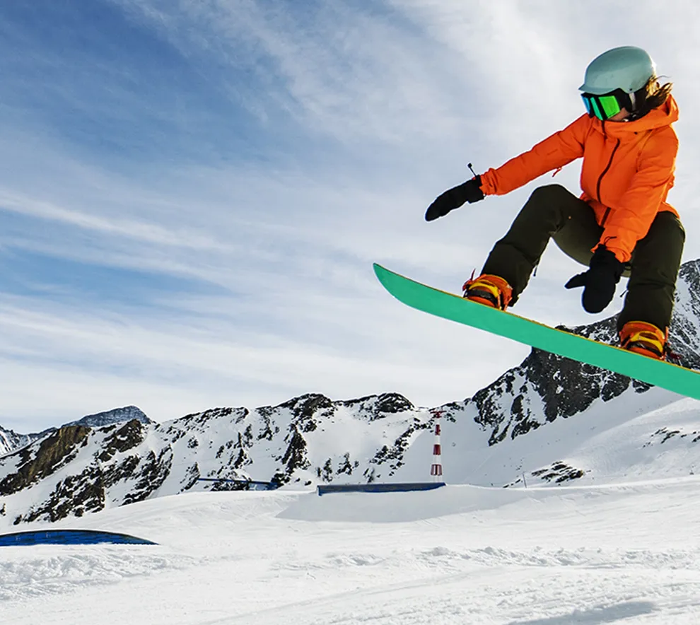 Snowboarder på vei ned fjellside med mye snø, sol og blå himmel