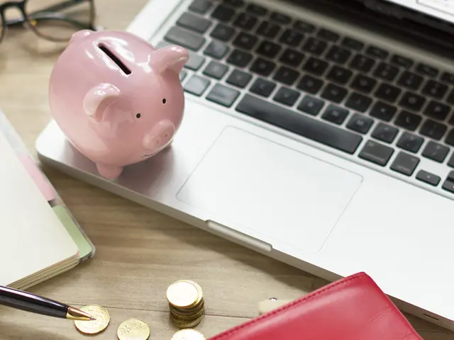 Rosa sparegris står på en laptop på et rotete kontorbord