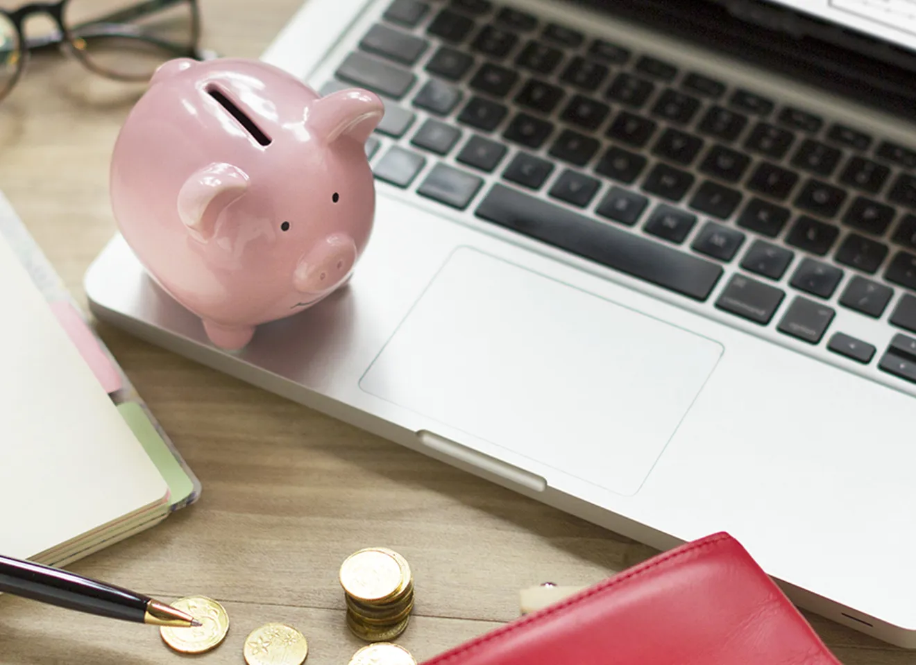 Rosa sparegris står på en laptop på et rotete kontorbord