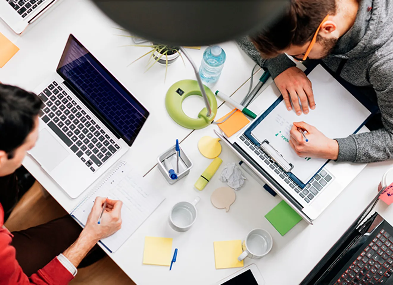 Oversiktsbilde av to menn som bruker laptopene sin til koding og skriving.