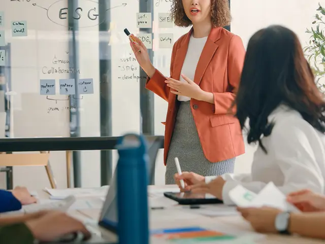 Et team diskuterer ESG-strategi mens en person presenterer foran en whiteboard.