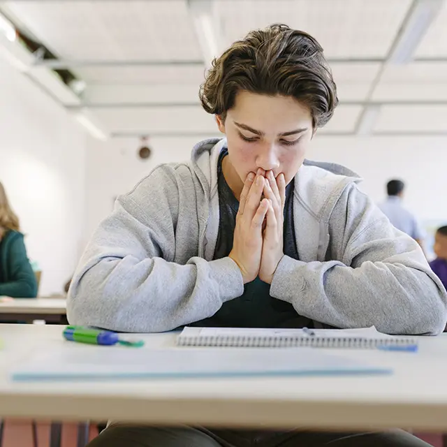 En ung gutt sitter ved pulten sin og virker fortvilt over en prøve eller et valg som må tas.