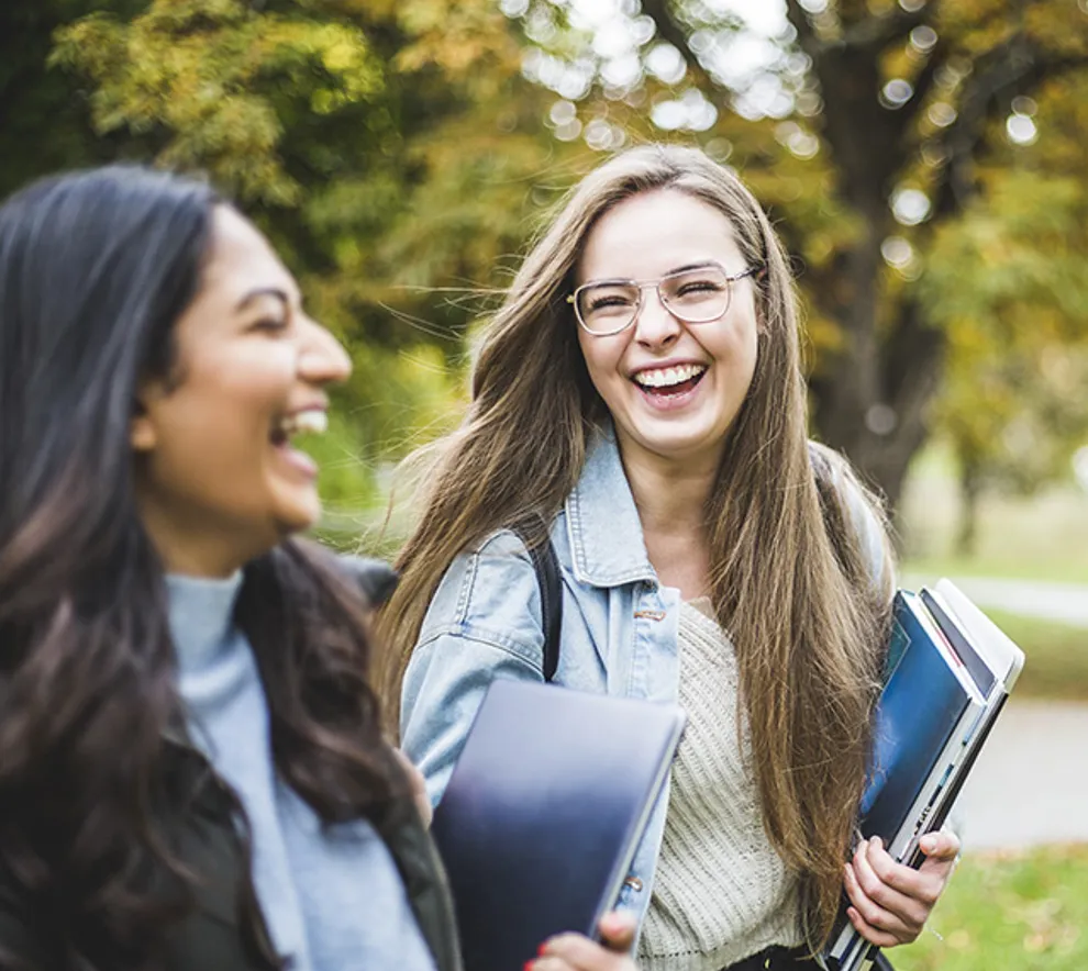 to unge jenter går ute ser på hverandre ler, har bøker i hendene