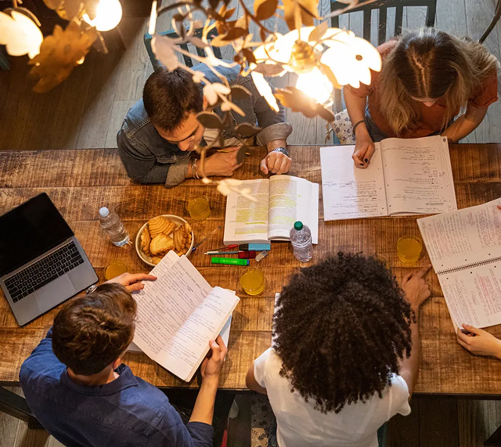 Studenter som studerer sammen rundt et bord med bøker, notater og laptop.