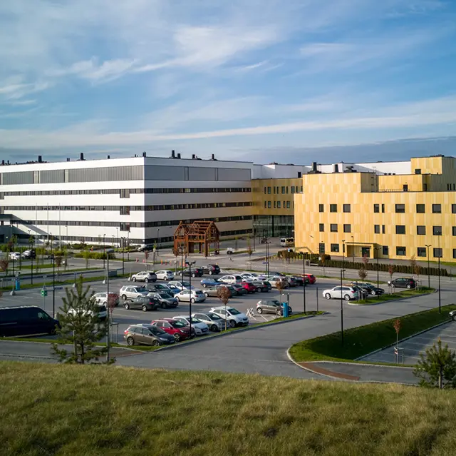Moderne sykehusbygg med parkeringsplass utenfor på solskinnsdag.