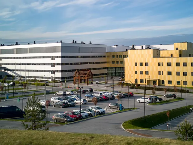 Moderne sykehusbygg med parkeringsplass utenfor på solskinnsdag.