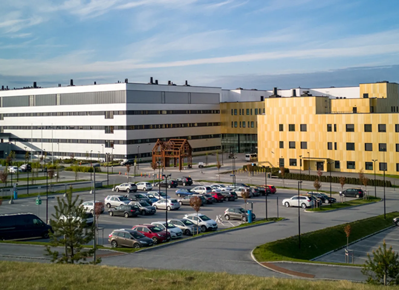 Moderne sykehusbygg med parkeringsplass utenfor på solskinnsdag.