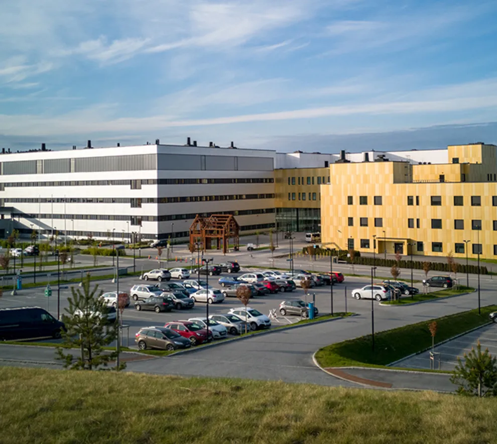 Moderne sykehusbygg med parkeringsplass utenfor på solskinnsdag.