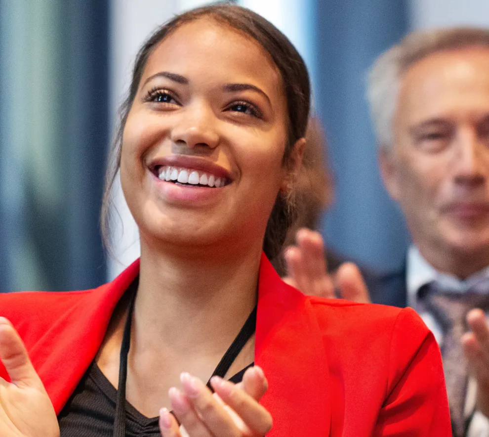 En kvinne i publikum klapper og smiler med andre mennesker rundt.