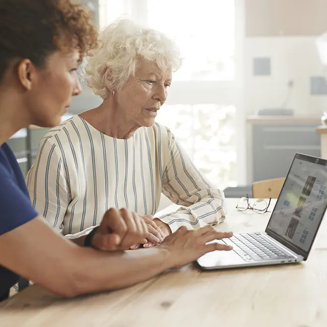 Helsearbeider hjelper eldre kvinne med å bruke datamaskin hjemme.