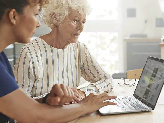 Helsearbeider hjelper eldre kvinne med å bruke datamaskin hjemme.