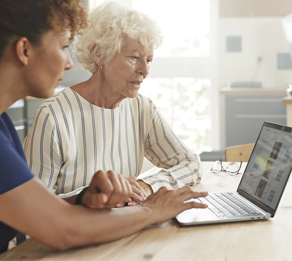 Helsearbeider hjelper eldre kvinne med å bruke datamaskin hjemme.