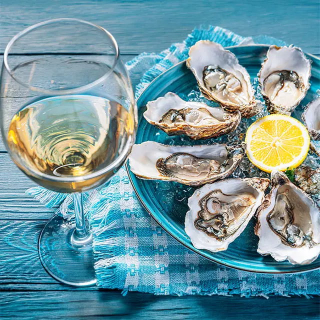 Nærbilde av østers på tallerken med en sitron, hvitvinsglass