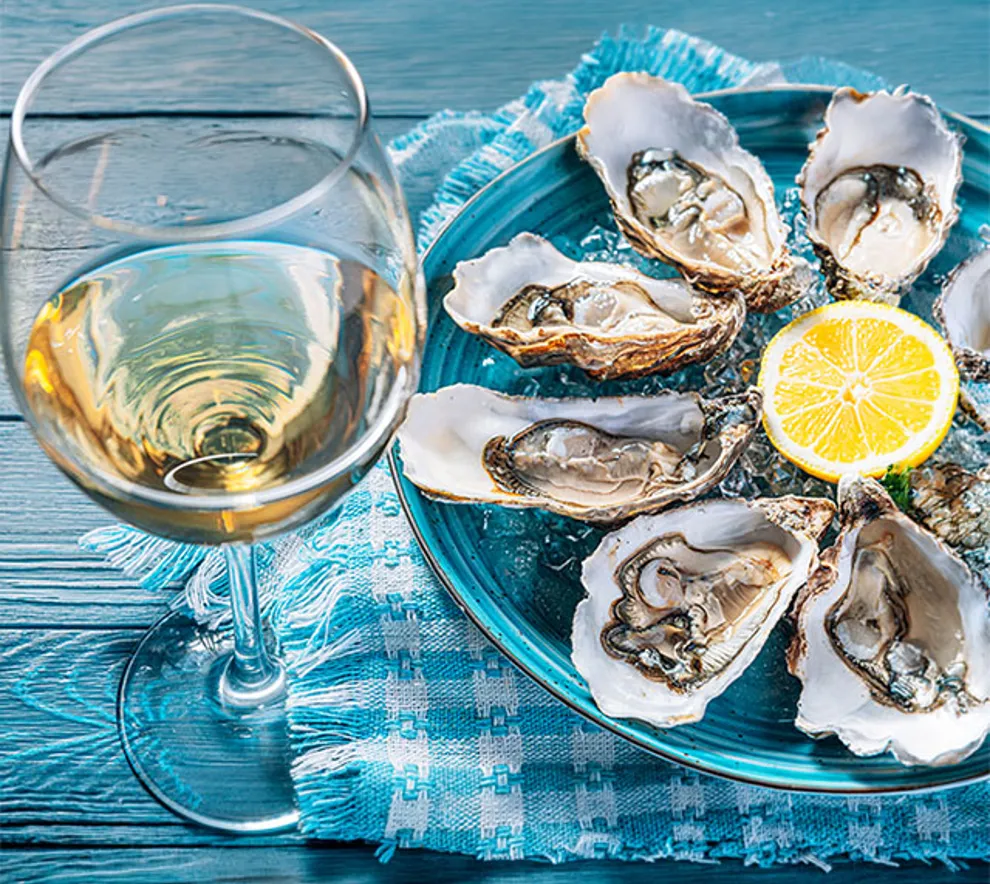 Nærbilde av østers på tallerken med en sitron, hvitvinsglass