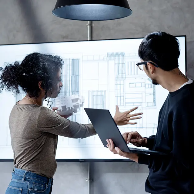 To personer samarbeider om digital bygningsmodell på skjerm med laptop og 3D-modell.