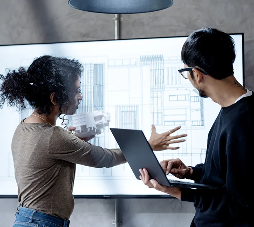 To personer samarbeider om digital bygningsmodell på skjerm med laptop og 3D-modell.
