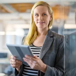 Voksen kvinne lener seg en glassvegg med et nettbrett i hendene