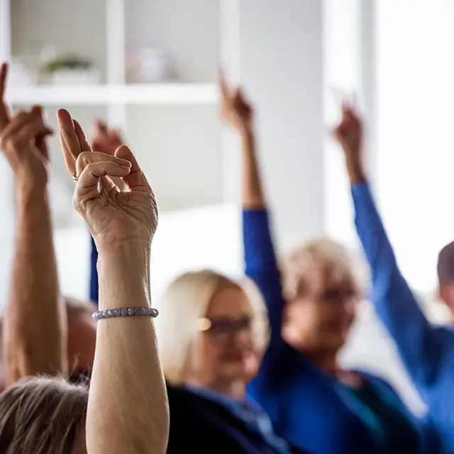 Personer rekker hendene i været under et møte eller en avstemning.