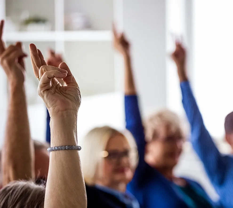 Personer rekker hendene i været under et møte eller en avstemning.