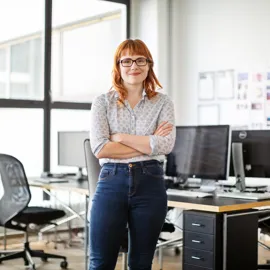 Ung kvinne står i kontorlandskap og smiler til kamera
