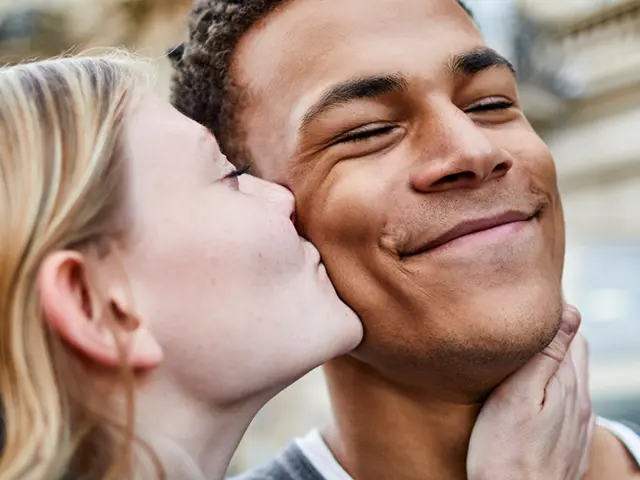 Ung kvinne kysser kjæresten sin på kinnet