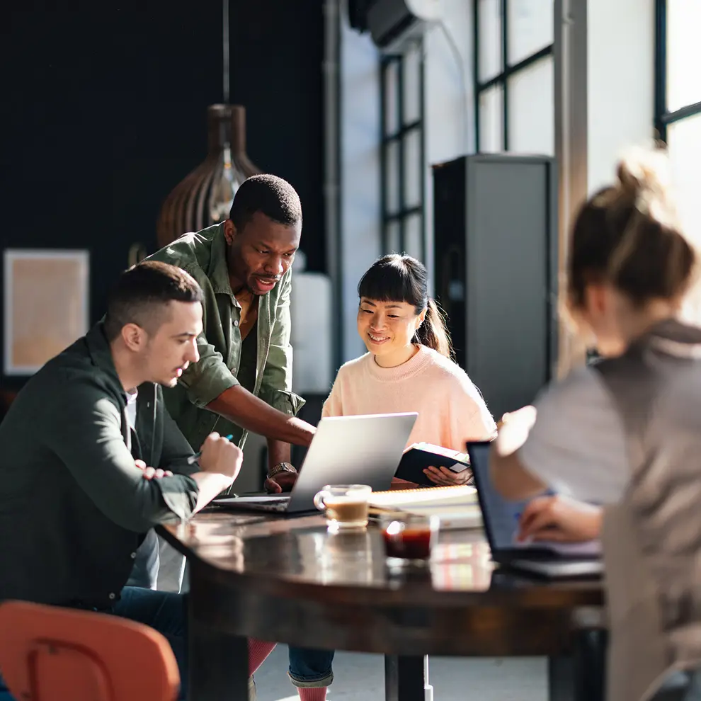Gruppe utviklere samarbeider rundt laptop med kaffe i uformell setting