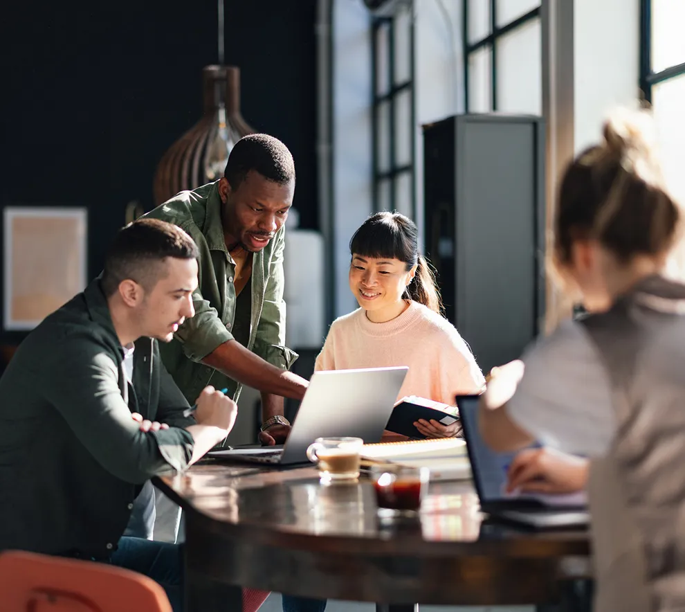 Gruppe utviklere samarbeider rundt laptop med kaffe i uformell setting