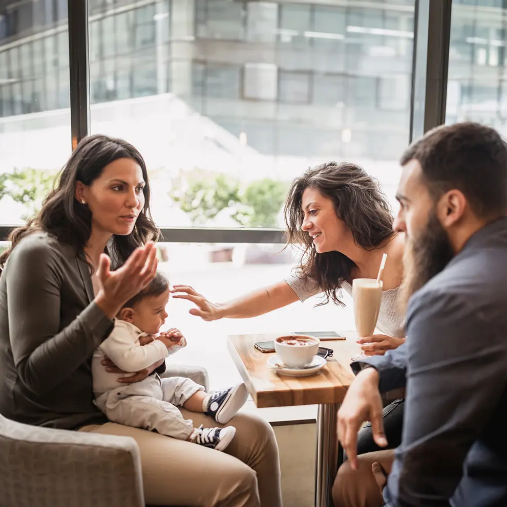Tre foreldre med baby møtes på kafé under barseltreff og drikker kaffe sammen