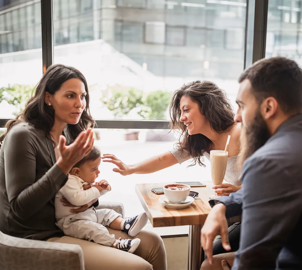 Tre foreldre med baby møtes på kafé under barseltreff og drikker kaffe sammen