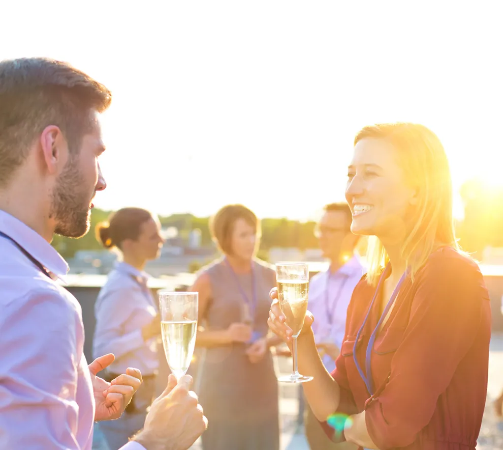 Kollegaer som snakker sammen og drikker champagne på en sommerfest i solnedgang.