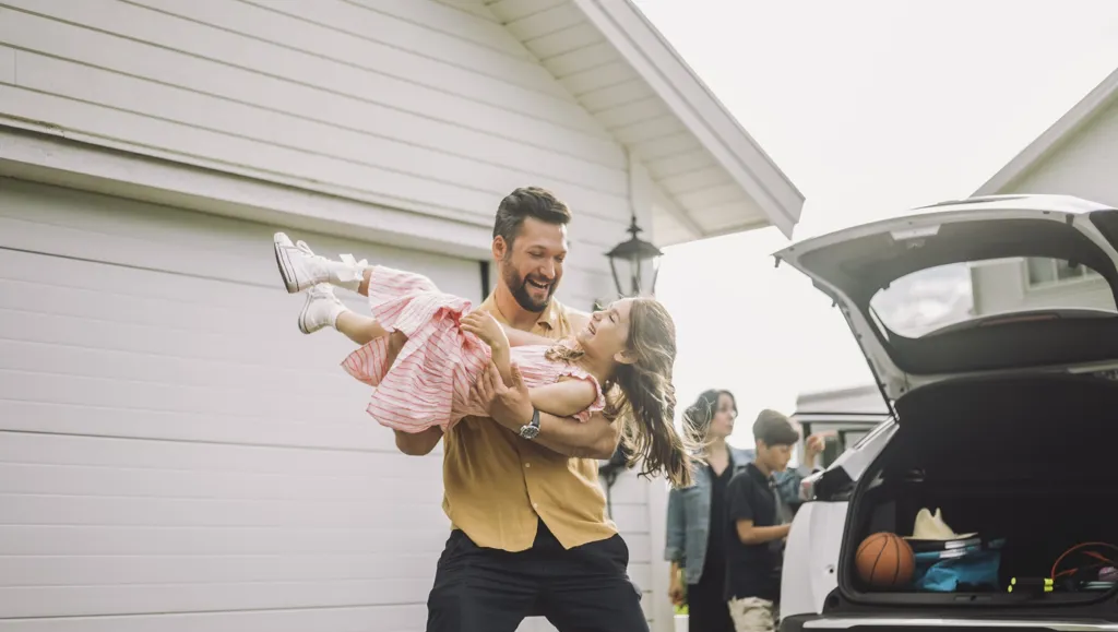 En far som holder sin datter i armene og begge ler i en hverdagssituasjon