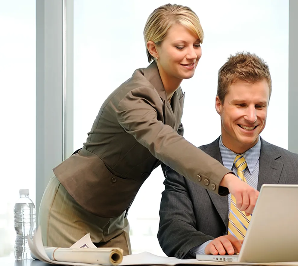 Foto av to kvinner og en mann som ser på en laptop på et møterom