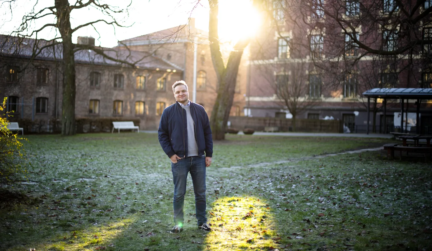 Håvard Solheim står foran et tre i en liten park foran noen byggninger